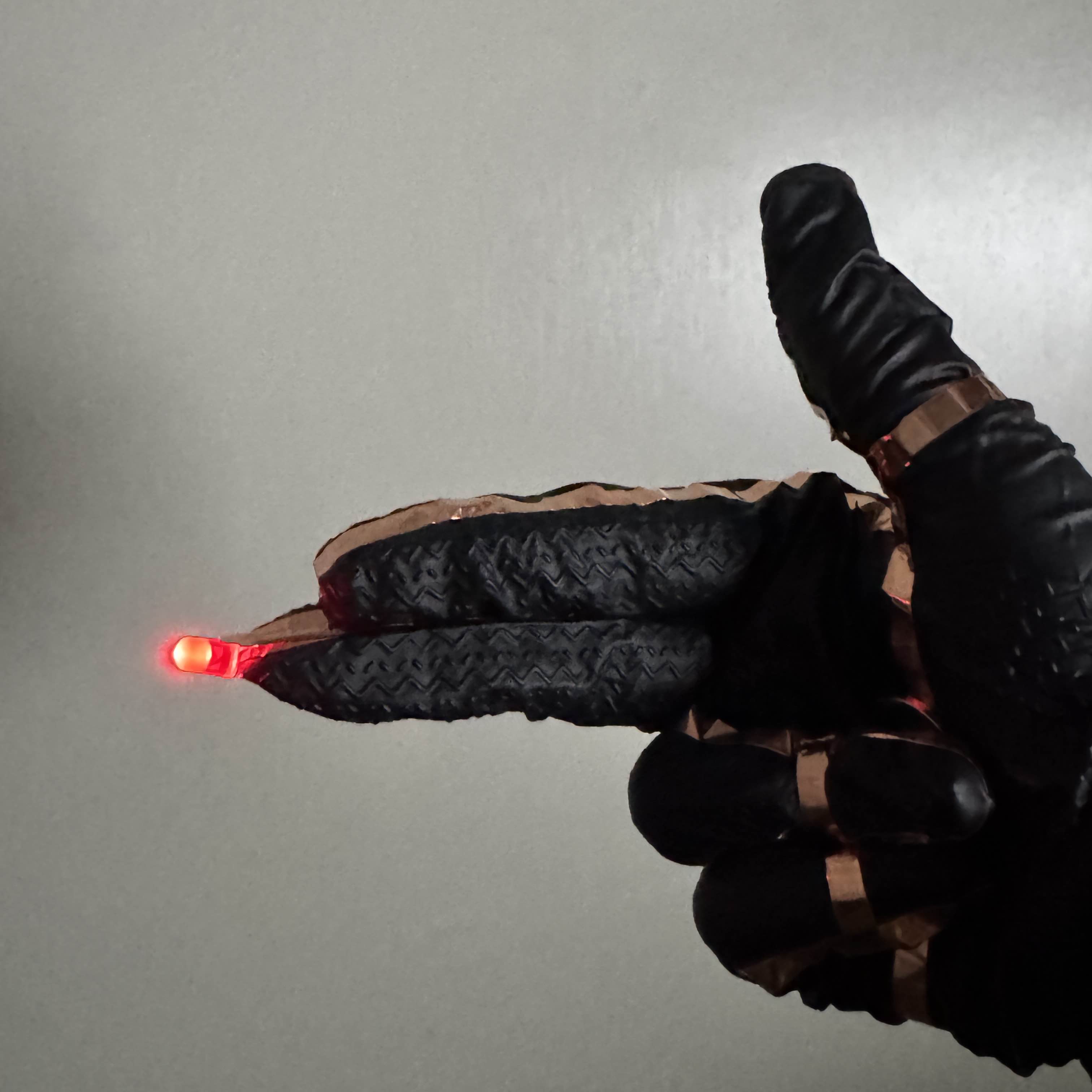 This finger gun glove works by using copper tape, a battery, and a red LED. To complete the circuit, the user must put their index and middle fingers together and bring their ring finger to the battery on their palm. This was done by breaking the tape between the index and middle fingers, and using the ring finger's tape as the positive wire for the battery. Most of the tape on the thumb and pinky finger is decorative for continuity and a futuristic feel.